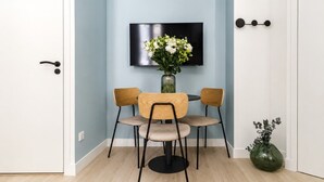 Et værelse med et spisebord og stole, et vægmonteret fladskærms-tv og en vase med blomster på gulvet.
