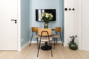 Ein Zimmer mit Esstisch und Stühlen, einem an der Wand befestigten Flachbildfernseher und einer Vase mit Blumen auf dem Boden.