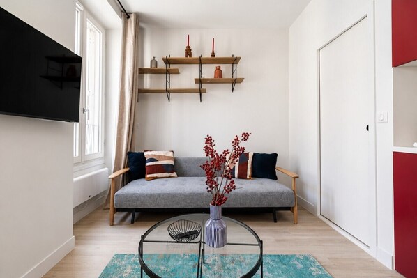A living room with a grey sofa, a round glass coffee table, and a wall-mounted TV. - Lavie Maison: Welcoming Apartment in Montmartre (Paris)
