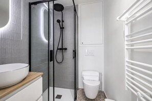 Een moderne badkamer met een douchecabine van glas, een witte wastafel en een toilet.