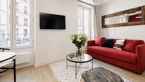 A modern living room with a red sofa, a glass coffee table, and a flat-screen TV mounted on the wall. - Lavie Maison : Charming Studio near to Montmartre (Paris)