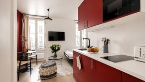 A compact kitchen with red cabinets, a black microwave, and a white countertop. - Lavie Maison : Charming Studio near to Montmartre (Paris)