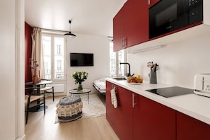 A compact kitchen with red cabinets, a black microwave, and a white countertop. - Lavie Maison : Charming Studio near to Montmartre (Paris)
