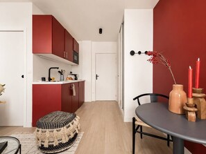A modern kitchen with red cabinets, a dining area with a round table, and a small stool. - Lavie Maison : Charming Studio near to Montmartre (Paris)