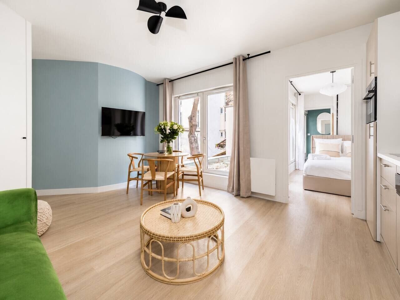 Un salon moderne doté d’un téléviseur à écran plat, d’une table basse ronde en osier, d’un canapé vert et d’un coin repas avec une table et des chaises.