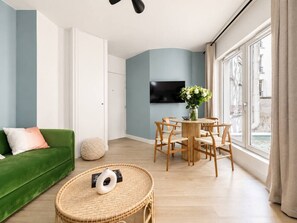 Ein modernes Wohnzimmer mit einem grünen Sofa, einem runden Kaffeetisch aus Weidwerk, einem Holzespeisesatz und einem Flachbildfernseher, der an einer blauen Wand angebracht ist.