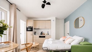 A compact hotel room with a bed, a green sofa, a dining area with a table and chairs, and a kitchenette. - Lavie Maison : Cozy Apartment near Montmartre (Paris)