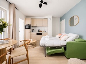 Ein kompaktes Hotelzimmer mit einem Bett, einem grünen Sofa, einer Essecke mit Tisch und Stühlen sowie einer Küchenzeile.