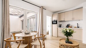 A modern kitchen with light wood cabinets, a dining area with a round table and chairs, and a wicker coffee table with a vase. - Lavie Maison : Cozy Apartment near Montmartre (Paris)