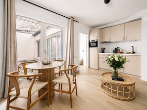Eine moderne Küche mit hellen Holzschränken, ein Essbereich mit rundem Tisch und Stühlen sowie ein Korbtisch mit einer Vase.
