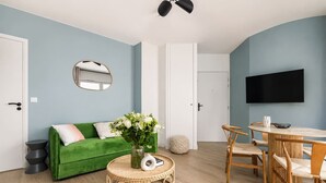 A living room with a green sofa, round coffee table, and a dining area with a table and chairs. - Lavie Maison : Cozy Apartment near Montmartre (Paris)
