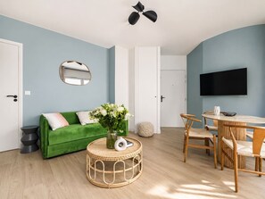 Ein Wohnzimmer mit einem grünen Sofa, einem runden Couchtisch und einem Essbereich mit Tisch und Stühlen.
