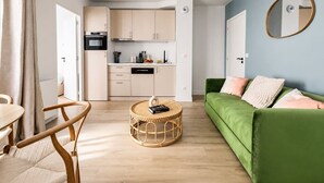 A modern living room with a green sofa, a round coffee table, and a kitchen area with light-colored cabinets. - Lavie Maison : Cozy Apartment near Montmartre (Paris)