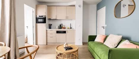 Un salon moderne avec un canapé vert, une table basse ronde et un coin cuisine doté de meubles de couleur claire.