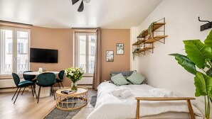 Una camera da letto moderna con un letto, un comodino e una TV. Si vedono anche poltrone, un tavolino e una pianta grande.