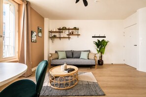 A modern living room with a grey sofa, a round wicker coffee table, and a potted plant. - Lavie Maison : Bright Apartment near Montmartre (Paris)