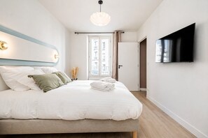 A modern bedroom with a bed, a flat-screen TV, a pendant light, and a view of the outside through a door. - Lavie Maison : Bright Apartment near Montmartre (Paris)