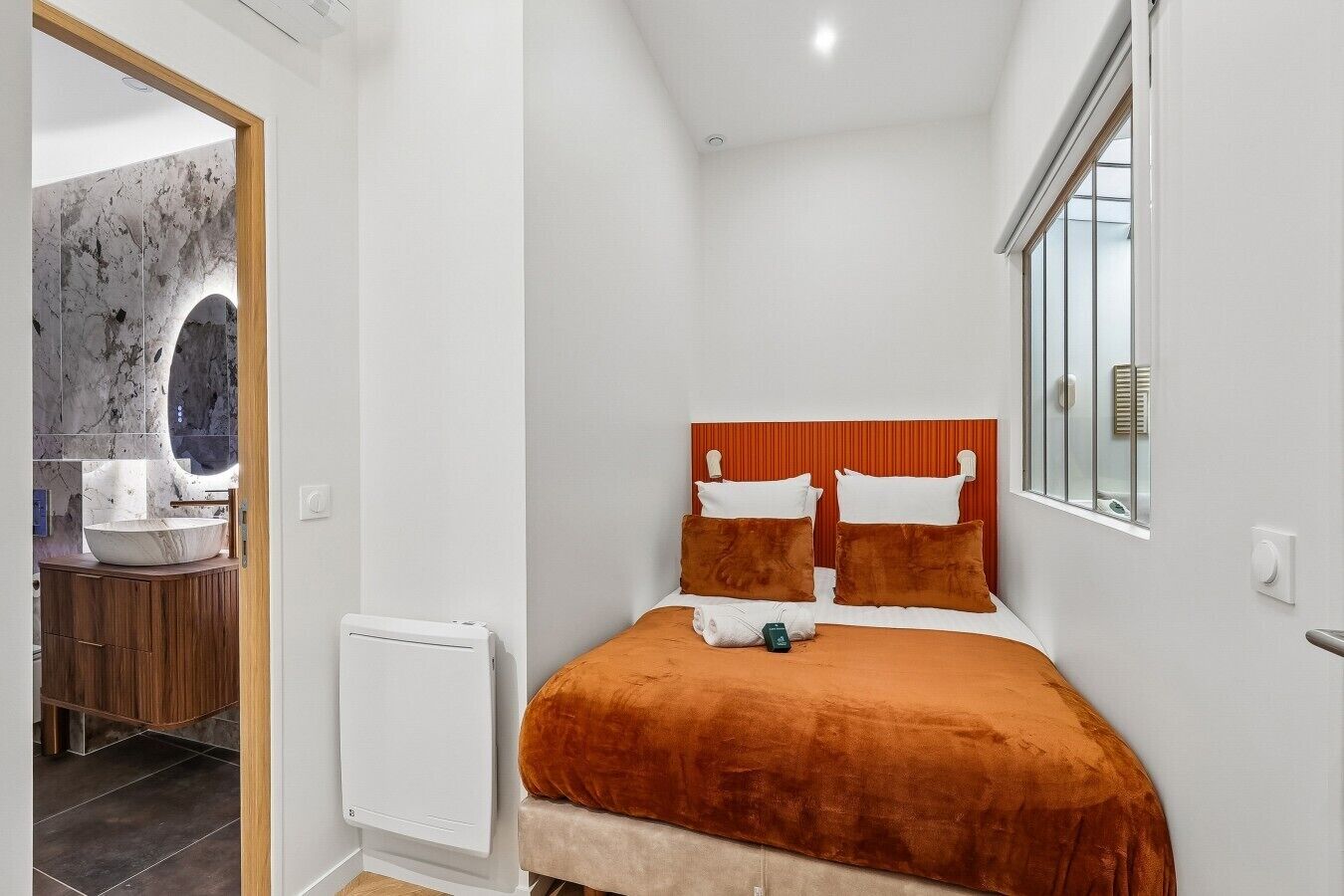 Un dormitorio con cama, mesita de noche, espejo y ventana.