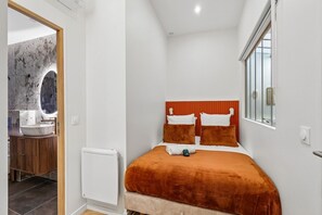 A bedroom with a bed, a bedside table, a mirror, and a window. - Lavie Maison | Central Paris – Le Marais (Paris)