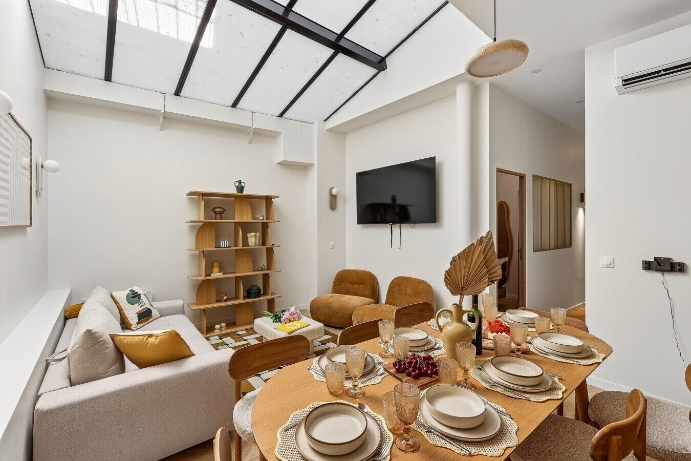 Ein modernes Wohnzimmer mit einer Couch, einem Holzregal, einem Esstisch für vier Personen und einem an der Wand befestigten Fernseher.
