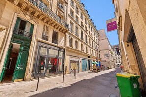 A street with buildings, a green trash bin, and a closed shop with a sign. - Lavie Maison | Central Paris – Le Marais (Paris)