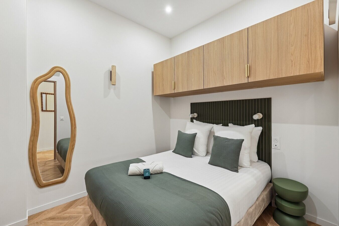 A bedroom with a bed, a mirror, and a wooden wardrobe.
