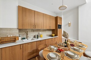 A modern kitchen with wooden cabinets, a white countertop, and a dining area set for a meal. - Lavie Maison | Central Paris – Le Marais (Paris)