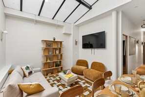 A modern living room with a sofa, chairs, a coffee table, and a TV mounted on the wall. - Lavie Maison | Central Paris – Le Marais (Paris)
