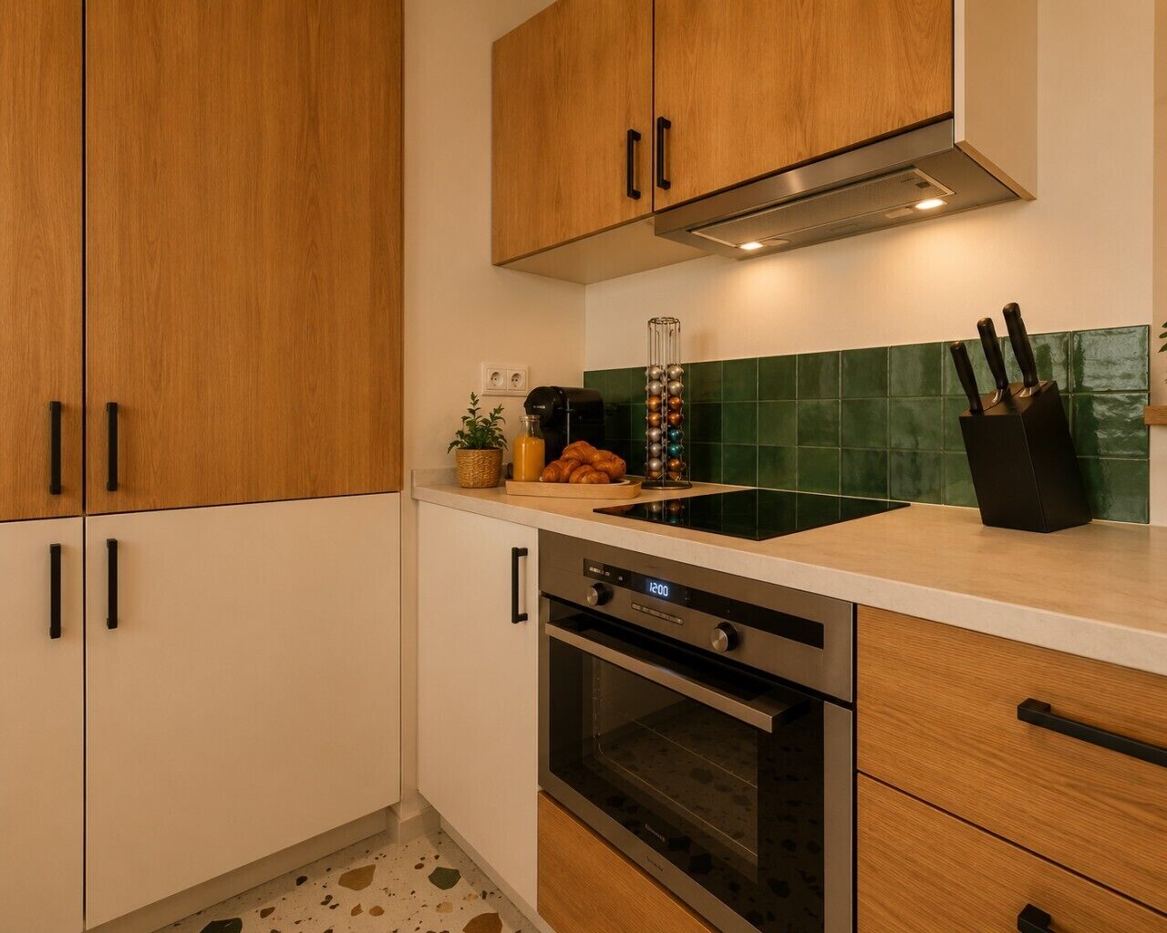Cocina con armarios de madera, horno de acero inoxidable, un lavamanos y salpicadero con azulejos verdes.