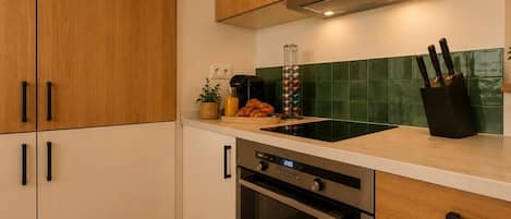 Cocina con armarios de madera, horno de acero inoxidable, un lavamanos y salpicadero con azulejos verdes.
