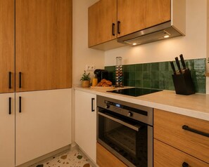 A kitchen with wooden cabinets, a stainless steel oven, a sink, and a green tiled backsplash. - Lavie Maison | Parisian living, Eiffel Tower (Paris)