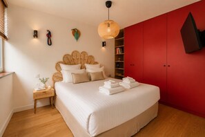 Een slaapkamer met een bed, nachtkastje, rode garderobe en hanglamp.