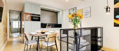 Una cocina moderna con armarios blancos, un comedor con una mesa redonda y sillas, y una escalera con barandilla negra.