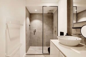 Un baño moderno con ducha de vidrio, un lavamanos grande de color blanco y un espejo.