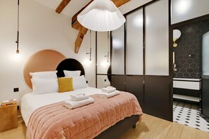 Ein modernes Schlafzimmer mit einem großen Bett, einem runden Kopfteil, einer hängenden Leuchte und einem Badezimmer mit schwarz-weißen Fliesen.