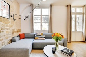 A modern living room with a grey sectional sofa, a round coffee table, a vase with flowers, and a framed picture on the wall. - Lavie Maison: Private Cinema in Le Marais (Paris)