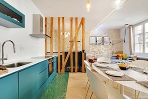 A modern kitchen with teal cabinets, a stone wall, and a dining area with a table set for four. - Lavie Maison: Private Cinema in Le Marais (Paris)