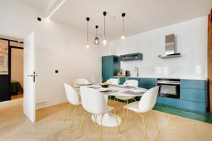 A modern kitchen with a dining area, white chairs, and a teal accent wall. - Lavie Maison: Private Cinema in Le Marais (Paris)