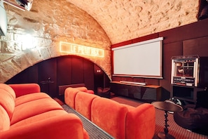 A cozy cinema room with plush orange seating, a large screen, and a popcorn machine. - Lavie Maison: Private Cinema in Le Marais (Paris)