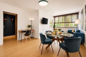 A modern dining area with a round glass table, blue chairs, and a breakfast setting. - Lavie Maison | Eiffel Tower & Beaugrenelle (Paris)