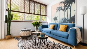 Ein Wohnzimmer mit blauem Sofa, einem Kaktus, einer Vase mit Blumen und einem Leopardenmuster-Teppich.