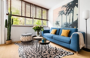 A living room with a blue sofa, a cactus, a vase with flowers, and a leopard print rug. - Lavie Maison | Eiffel Tower & Beaugrenelle (Paris)