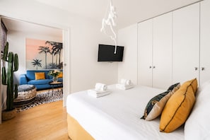 A hotel room with a bed, a television, a wardrobe, and a seating area with a blue sofa and a cactus plant. - Lavie Maison | Eiffel Tower & Beaugrenelle (Paris)