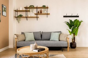 A living room with a grey sofa, a round wicker coffee table, a potted plant, and wall-mounted shelves with plants and decorative items. - Lavie Maison : Cozy Apartment in the city (Paris)