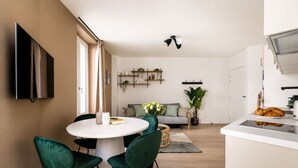 A modern kitchen with a white countertop, a built-in oven, and a dining area with a round table and green chairs. - Lavie Maison : Cozy Apartment in the city (Paris)