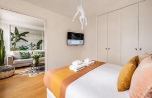 A modern hotel room with a bed, a flat-screen TV, a wardrobe, and a large window with plants. - Lavie Maison | Eiffel Nearby - Beaugrenelle (Paris)