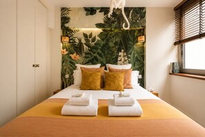 A hotel room with a bed, pillows, towels, a window with blinds, and a wall with a plant mural. - Lavie Maison | Eiffel Nearby - Beaugrenelle (Paris)
