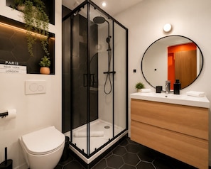 Ein modernes Badezimmer mit einer einteiligen Duschkabine, einer weißen Toilette, einem Holzwaschtisch und einem runden Spiegel.