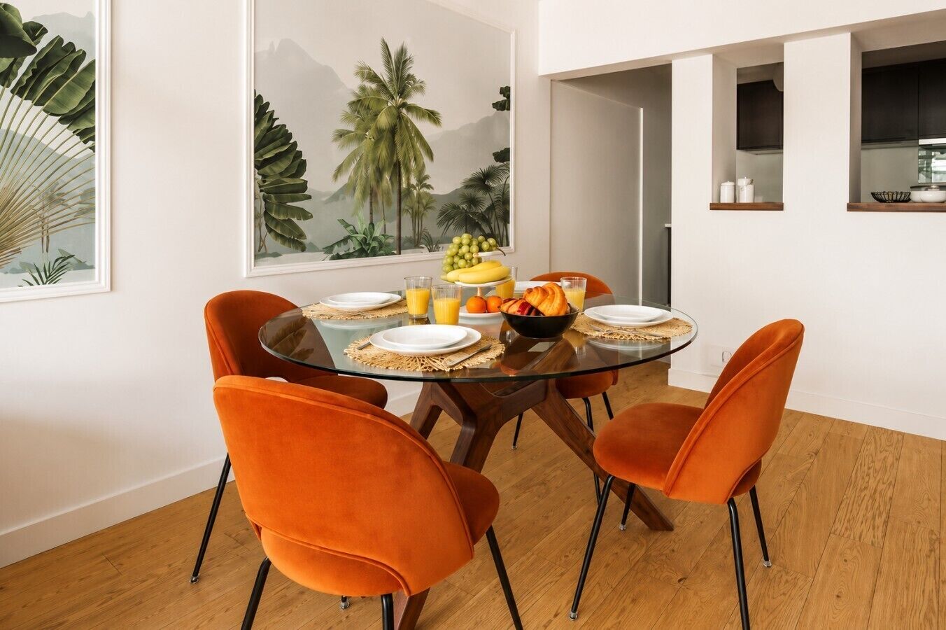 Un comedor con una mesa de vidrio, sillas color naranja y un mural temático tropical.
