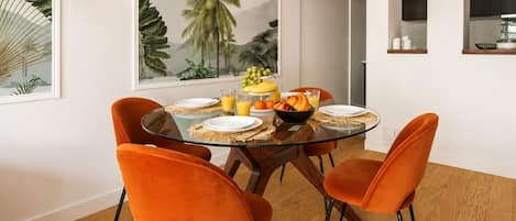 Un comedor con una mesa de vidrio, sillas color naranja y un mural temático tropical.